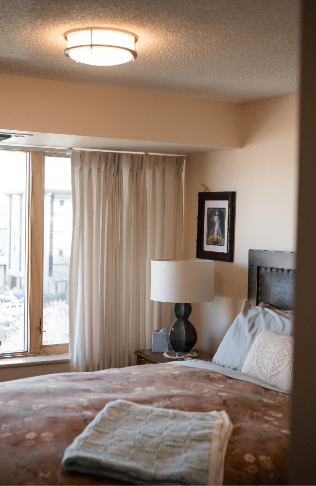 A ceiling light shines onto a bed in a Kavod Senior Life apartment